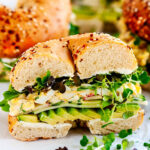 Avocado Egg Salad Bagel Sandwich half on parchment and white marble side view