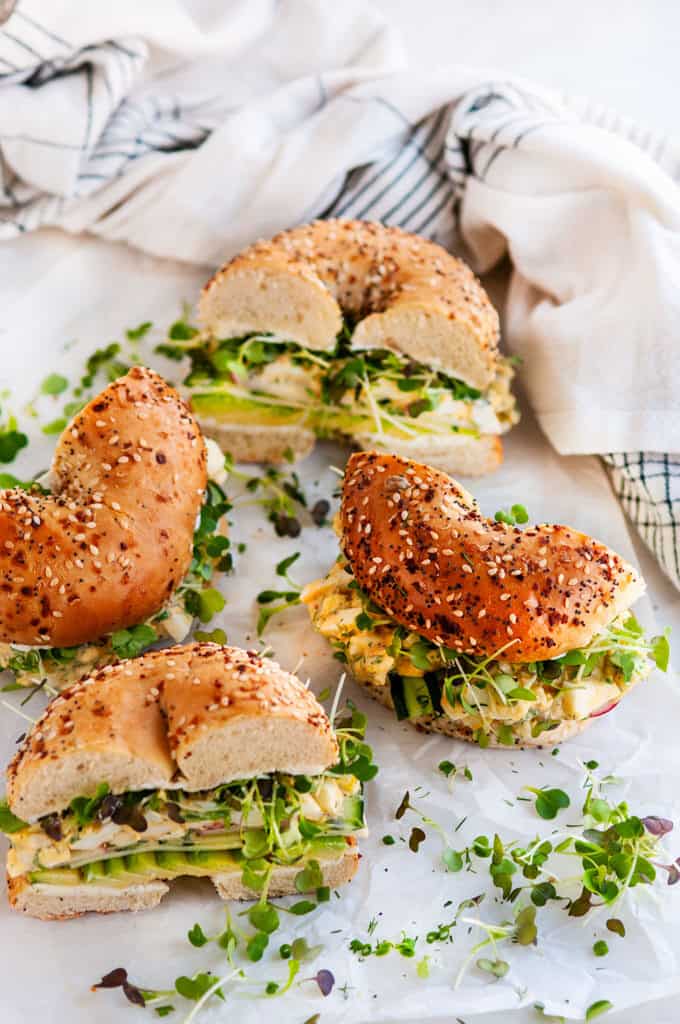 Avocado Egg Salad Bagel Sandwich halves on parchment and white marble