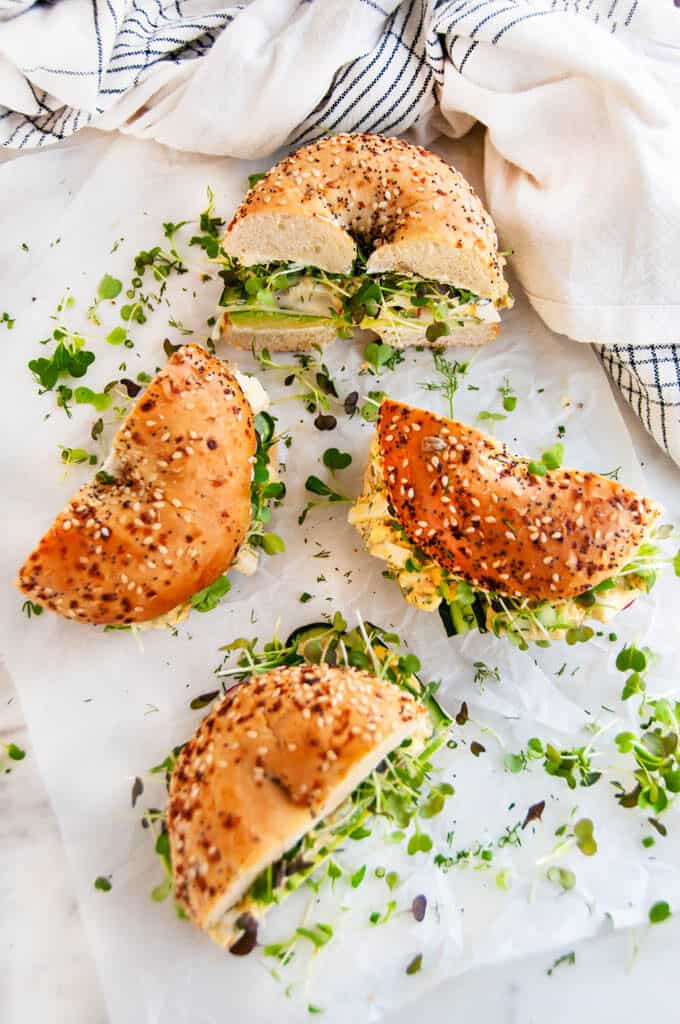Avocado Egg Salad Bagel Sandwich halves on parchment and white marble