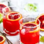 Blood Orange Margaritas on the rocks with limes and tea towel on white marble