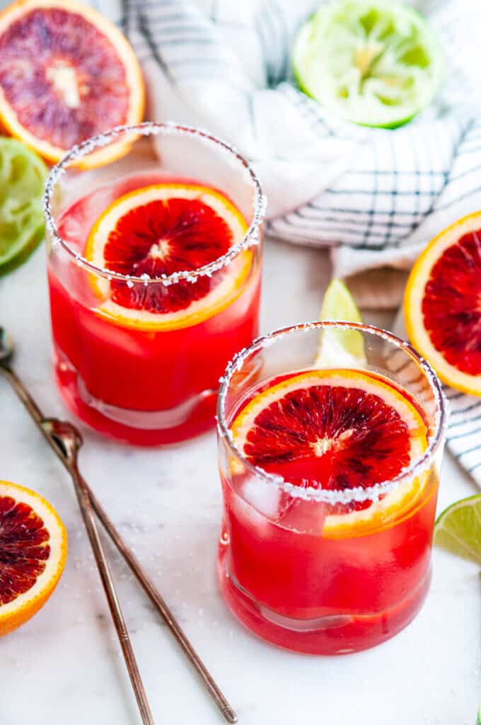 Blood Orange Margaritas on the rocks with limes and tea towel on white marble