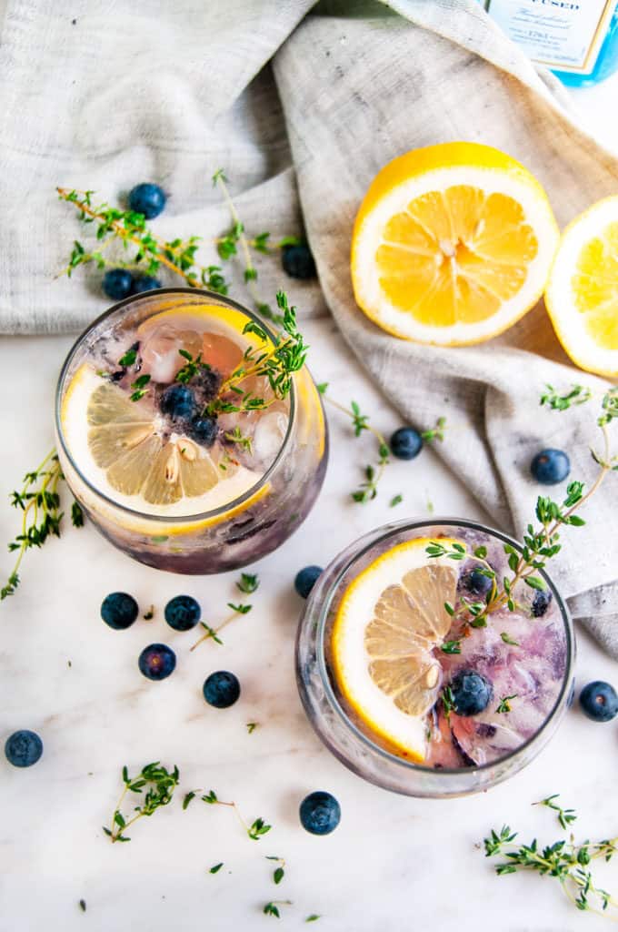 Blueberry Thyme Gin Fizz with lemons and gray tea towel on white marble