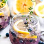 Blueberry Thyme Gin Fizz with lemons and gray tea towel on white marble