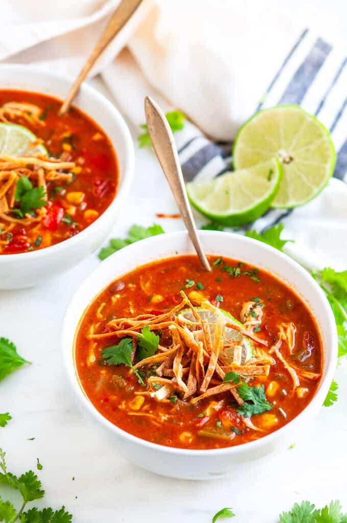Slow Cooker Chicken Enchilada Soup with tortilla strips, lime and cilantro in white bowls on white marble