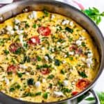 Greek Vegetable Frittata in all-clad skillet with oregano and tea towel on white marble