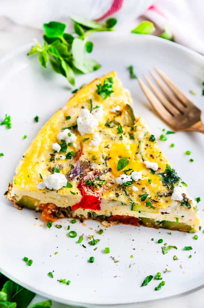 Greek Vegetable Frittata slice with gold fork and tea towel on white plate