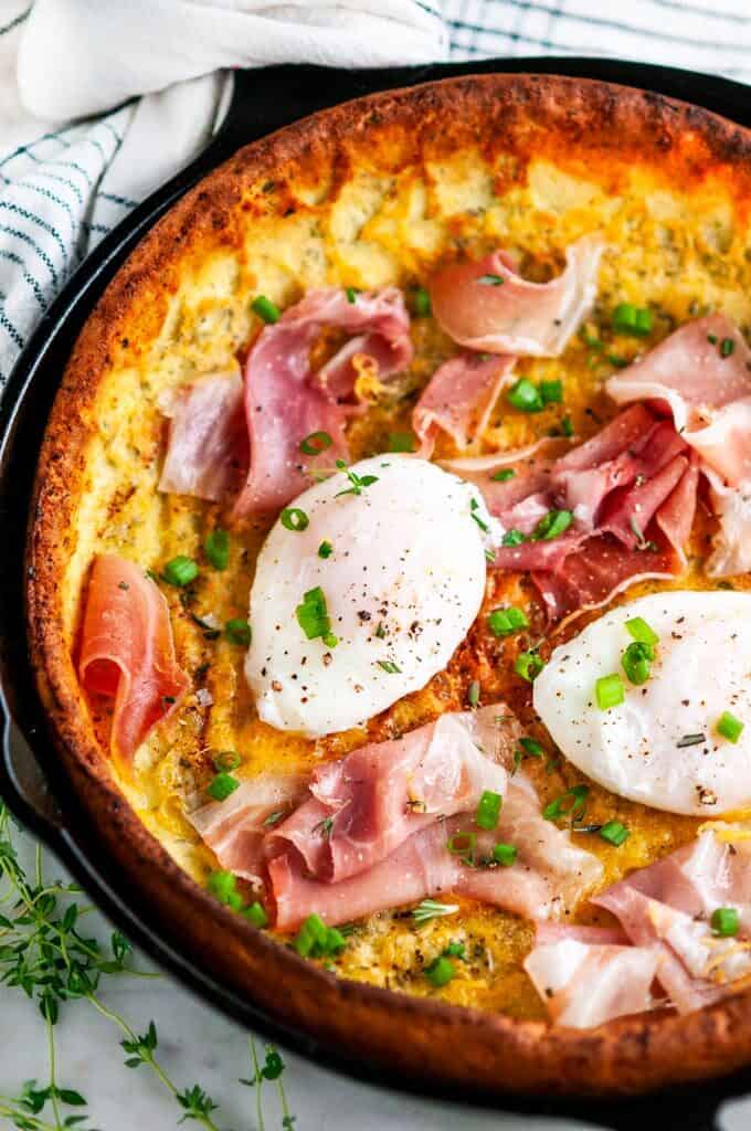 Savory Herb Cheddar Dutch Baby with poached eggs and prosciutto in lodge cast iron skillet
