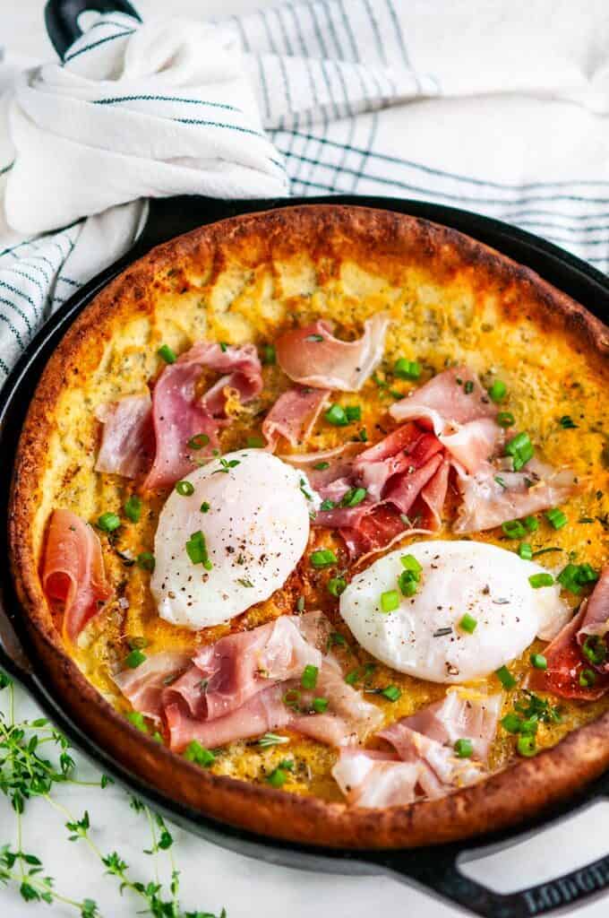 Savory Herb Cheddar Dutch Baby with poached eggs and prosciutto in lodge cast iron skillet with tea towel