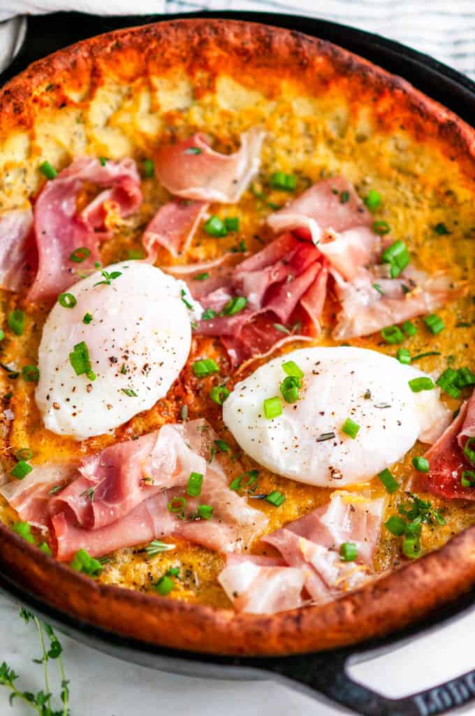 Savory Herb Cheddar Dutch Baby with poached eggs and prosciutto in lodge cast iron skillet close up