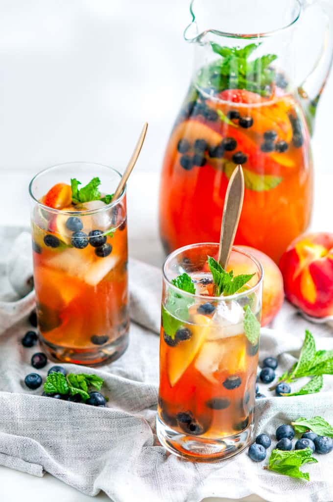 Sparkling Arnold Palmer Sangria pitcher and glasses with blueberries, peaches, mint, and gold spoons