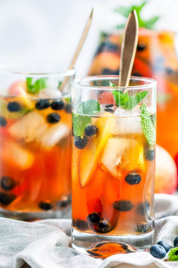 Sparkling Arnold Palmer Sangria pitcher and glasses with blueberries, peaches, mint, and gold spoons