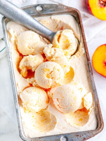 No Churn Peaches and Cream Ice Cream with gray scoop and tea towel on white marble