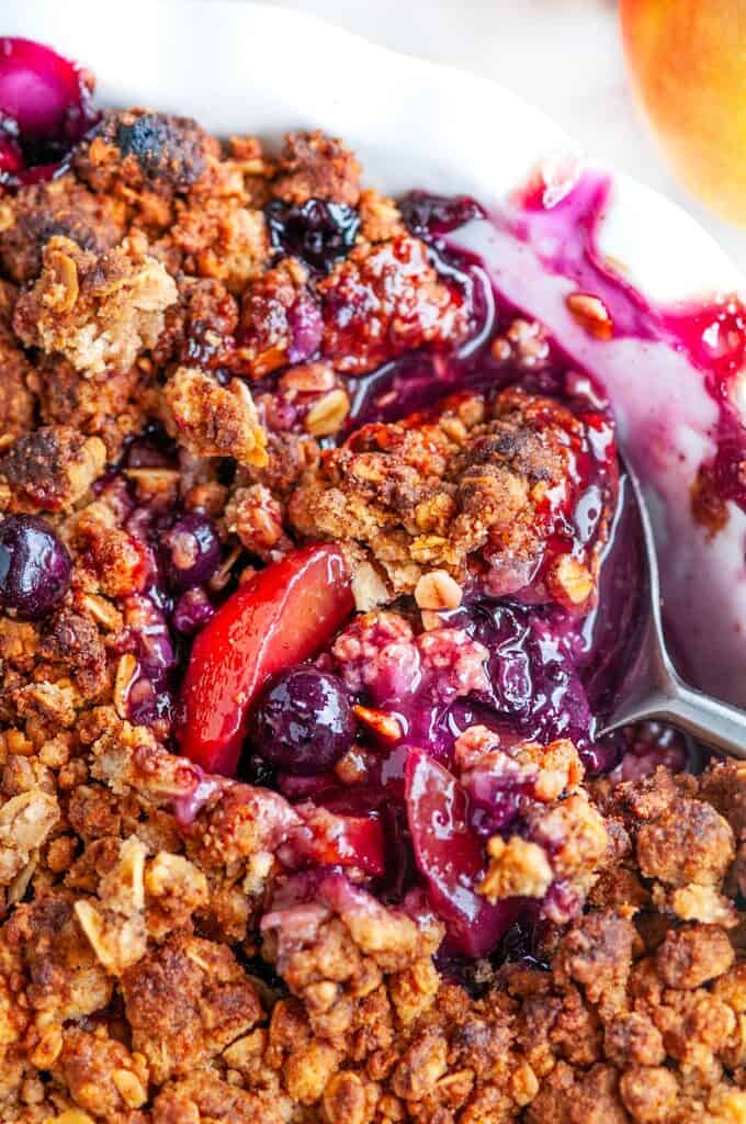 Easy Peach Blueberry Crisp in white pie pan with serving spoon close up