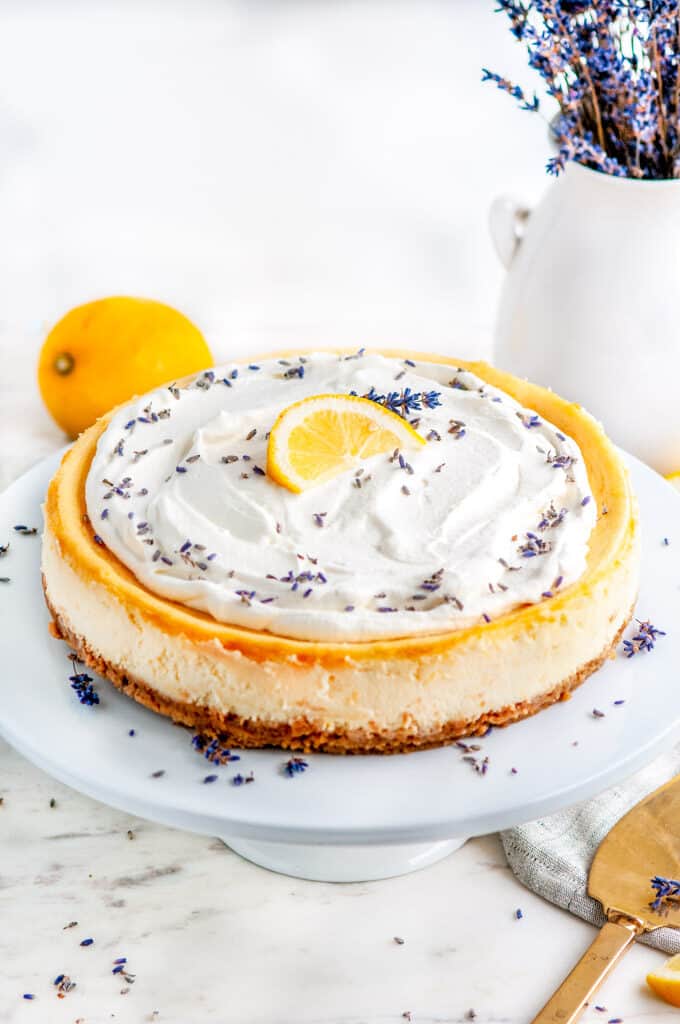 Lemon Lavender Mascarpone Cheesecake on white cake stand with tea towel and gold server
