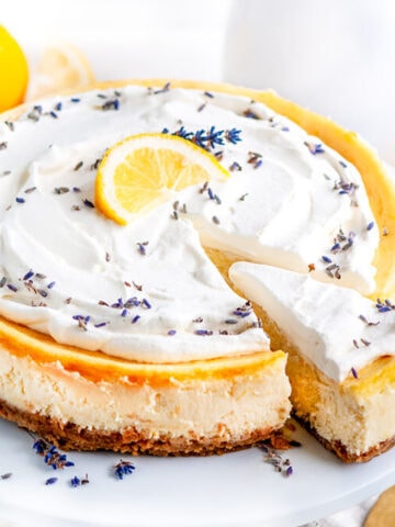 Lemon Lavender Mascarpone Cheesecake on white cake stand with slice and gold server