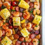 Sheet Pan Shrimp Boil with potatoes, andouille sausage, and corn on white marble