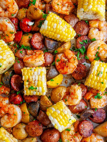 Sheet Pan Shrimp Boil with potatoes, andouille sausage, and corn on white marble