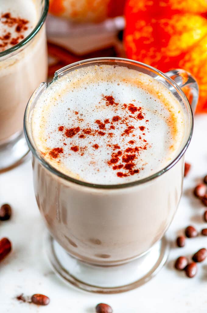 Pumpkin Spice Latte (with real pumpkin!) in glass mug close up with coffee beans on white marble