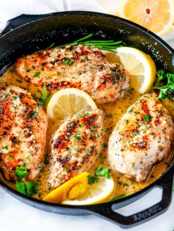 Skillet lemon garlic butter chicken in lodge cast iron skillet with lemons and herbs on white marble