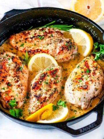Skillet lemon garlic butter chicken in lodge cast iron skillet with lemons and herbs on white marble