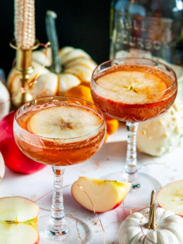 Autumn Apple Cider Whiskey Cocktail in glasses white marble with pumpkins