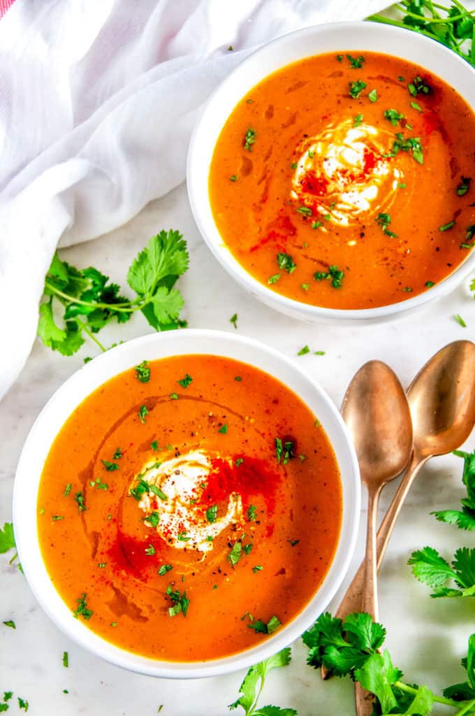 Carrot coriander soup in white bowls with gold spoons and fresh cilantro on white marble