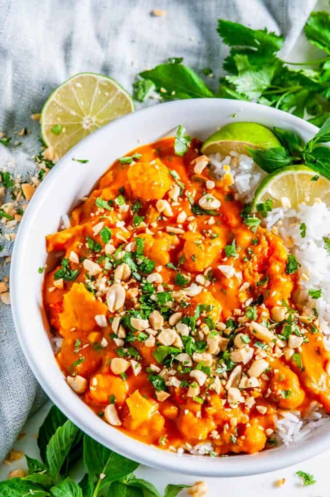 Caulfilower Sweet Potato Coconut Curry with jasmine rice, cilantro, and limes in white bowl on marble