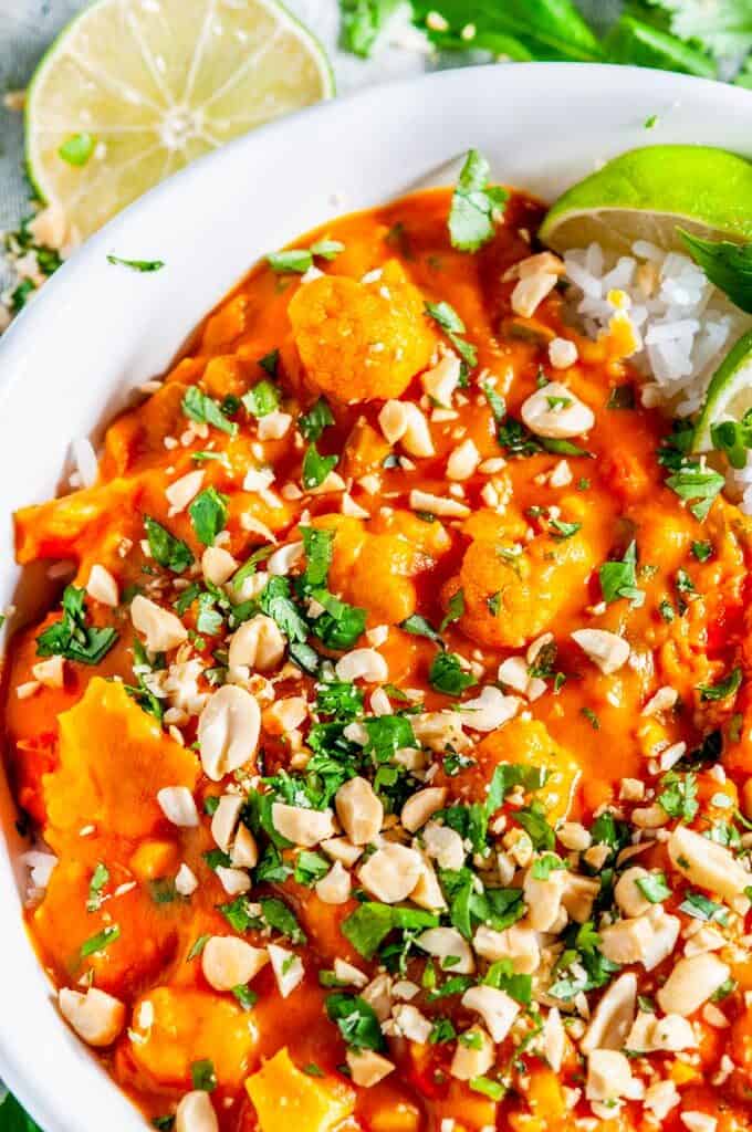 Caulfilower Sweet Potato Coconut Curry with jasmine rice, cilantro, and limes in white bowl on marble close up