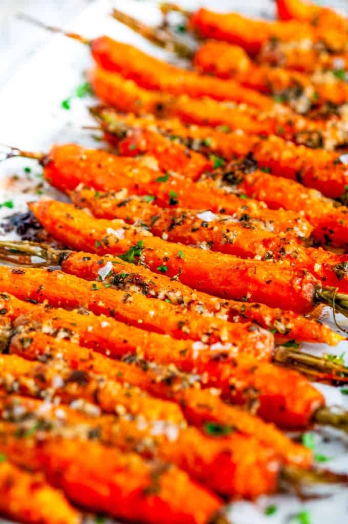 Garlic Parmesan Roasted Carrots with fresh parsley on parchment paper close up
