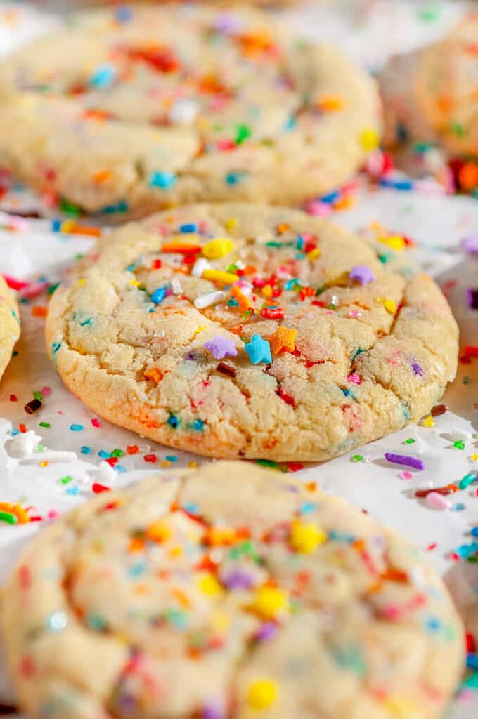 Soft Chewy Funfetti Cookies with rainbow sprinkles and sanding sugar on parchment paper close up