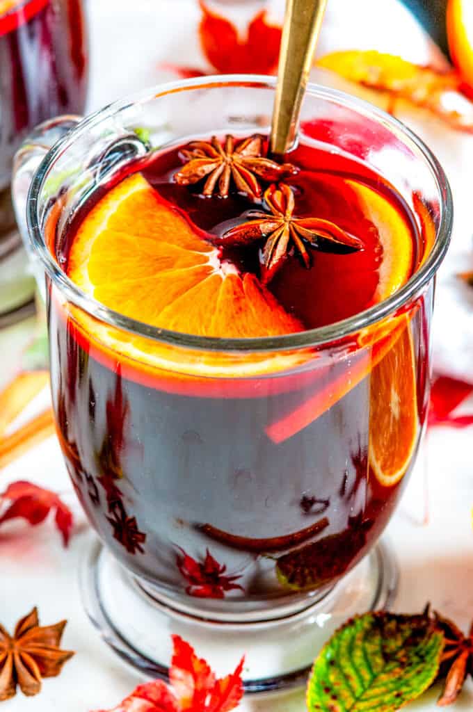 Spiced Holiday Mulled Wine in glass mug with gold spoon, orange slices, star anise, cinnamon sticks, and maple leaves close up