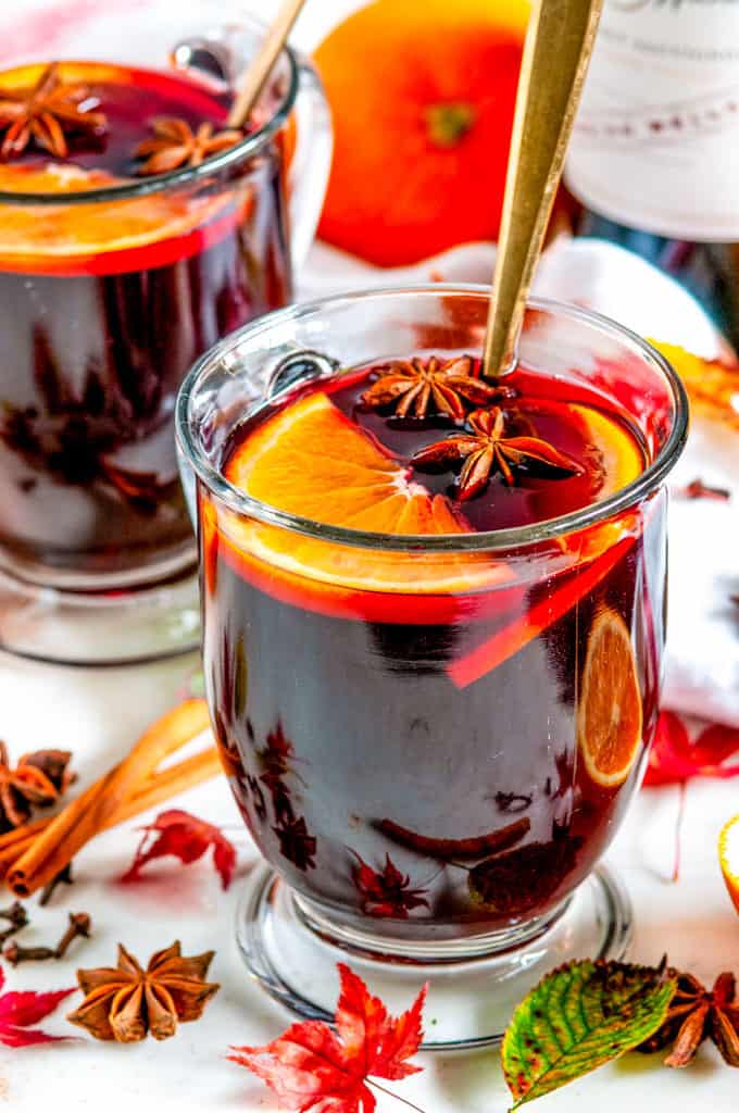 Spiced Holiday Mulled Wine in glass mugs with gold spoons, orange slices, star anise, cinnamon sticks, and maple leaves