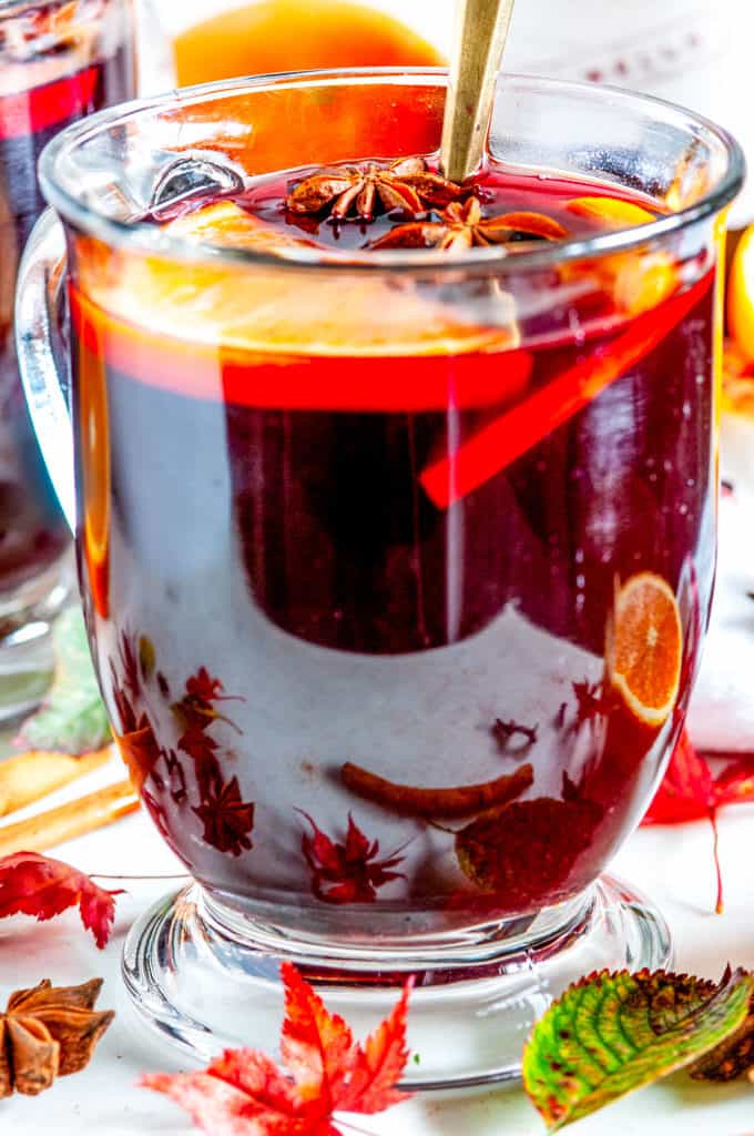 Spiced Holiday Mulled Wine in glass mug with gold spoon, orange slices, star anise, cinnamon sticks, and maple leaves close up
