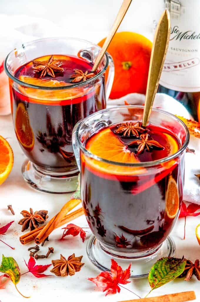 Spiced Holiday Mulled Wine in glass mugs with gold spoons, orange slices, star anise, cinnamon sticks, and maple leaves
