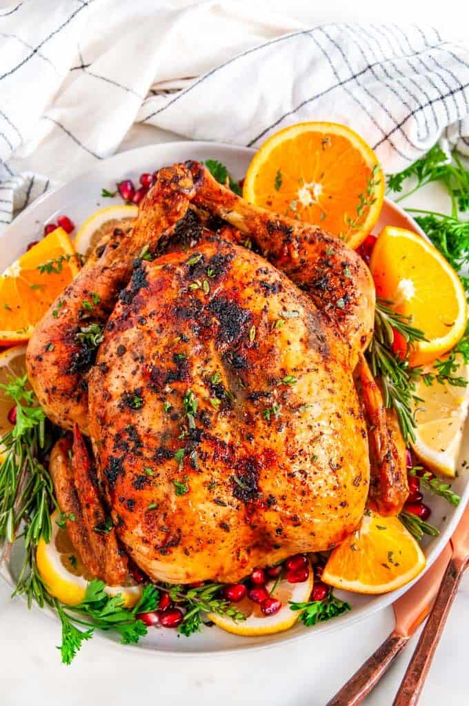 Herb Garlic Butter Roasted Turkey on white plate with oranges, lemons, herbs, and pomegranate arils
