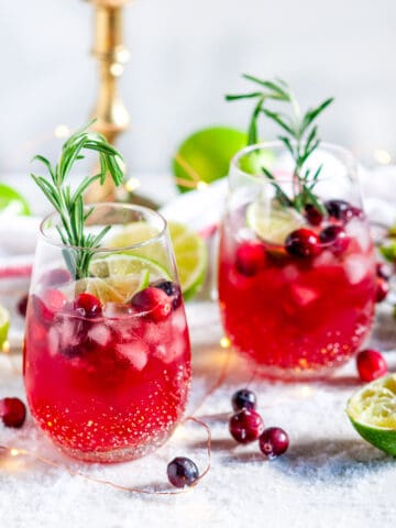 Yuletide Cranberry Moscow Mule with rosemary and limes on white marble with gold candle