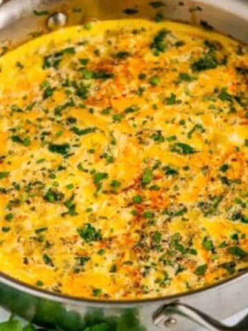 Swiss Cheese Cauliflower Frittata in all clad skillet on white marble with cilantro and tea towel