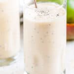 Banana Mango Coconut Smoothie in glasses with chia seeds and spoons om white marble close up