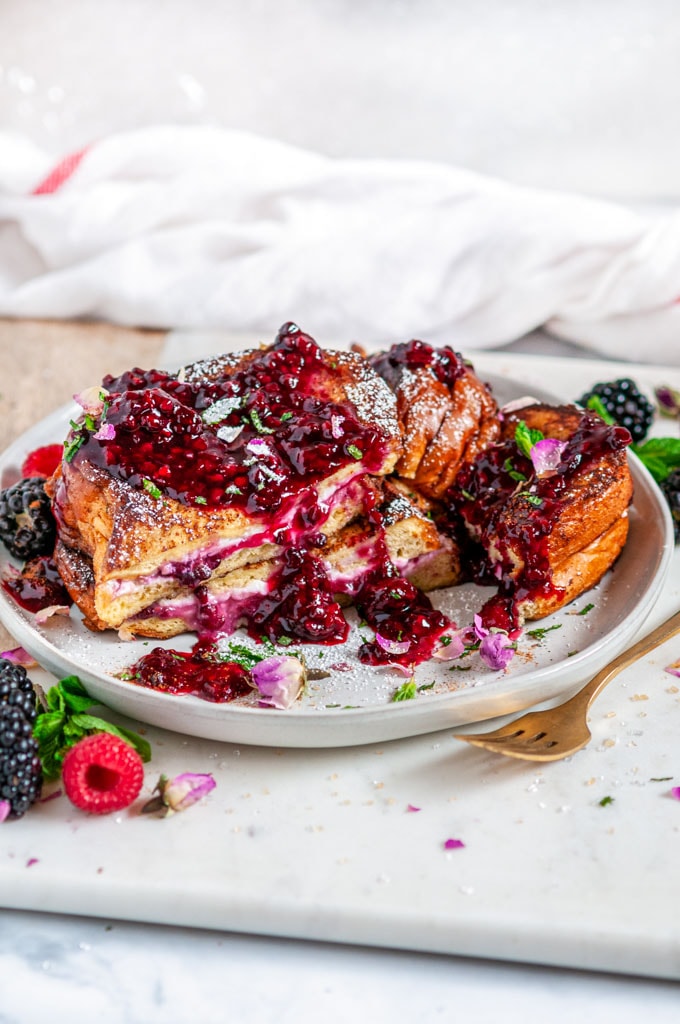 Cream Cheese Stuffed Blackberry Compote French Toast on gray plate and white marble with flowers and gold fork