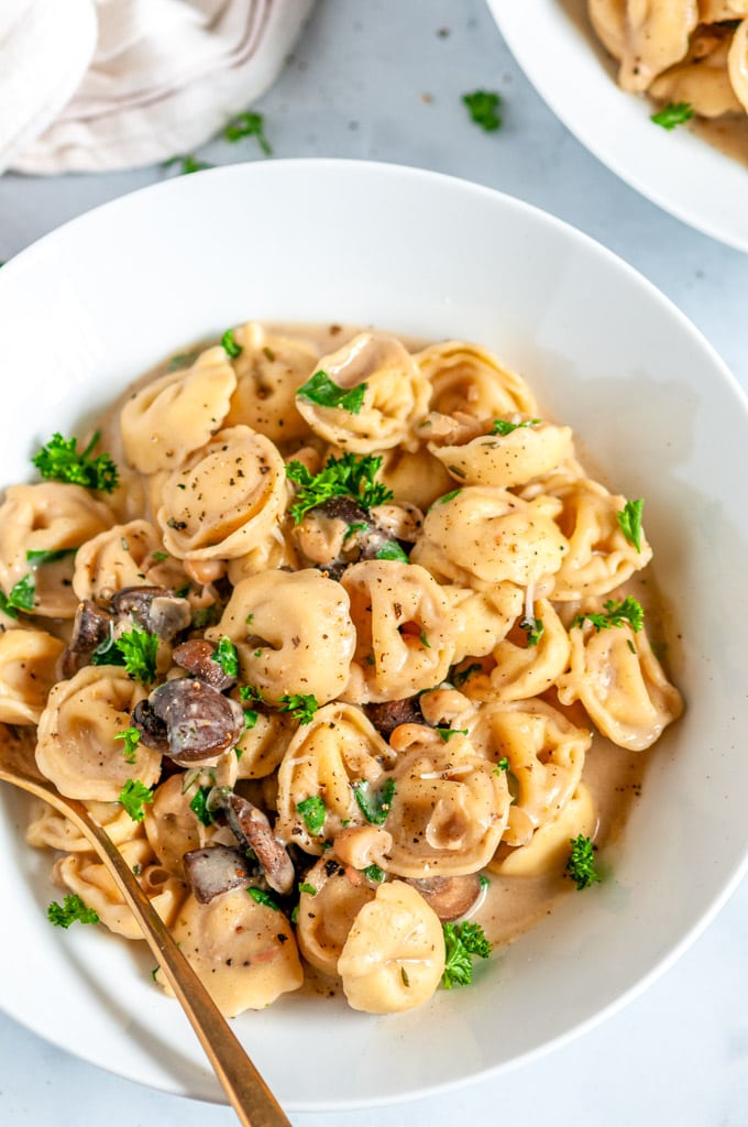 One Pot Creamy White Bean Tortellini with mushrooms and gold spoon in white bowl