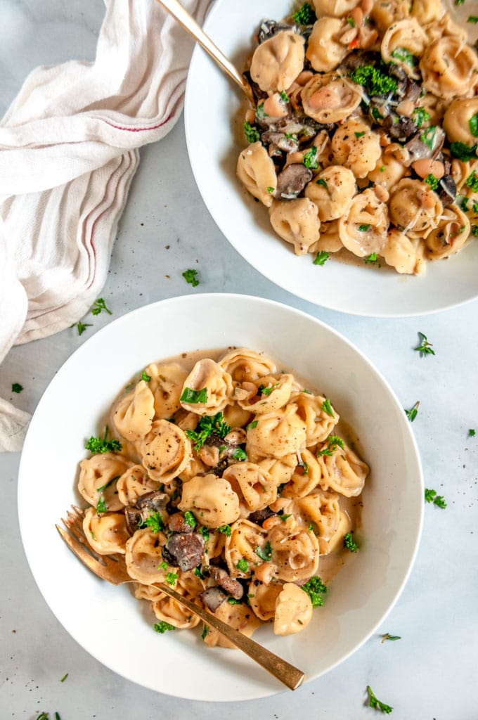 One Pot Creamy White Bean Tortellini with mushrooms and gold spoon in white bowl