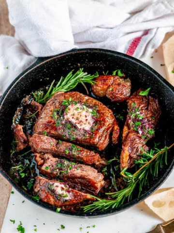 Rib Eye Steak with Red Wine Shallot Compound Butter and herbs sliced in cast iron skillet