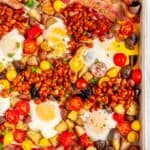 Sheet Pan Full English Breakfast with sausage, bacon, eggs, tomatoes, baked beans, and potatoes on white marble