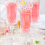 Sparkling Raspberry Rose Spritzer in crystal sugar rimmed glasses with variegated lemon slices on white marble