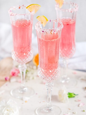 Sparkling Raspberry Rose Spritzer in crystal sugar rimmed glasses with variegated lemon slices on white marble