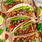 Instant Pot Chicken Tinga tacos with avocado, limes, red onion and cilantro on brown parchment over head