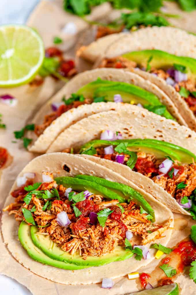 Instant Pot Chicken Tinga tacos with avocado, limes, red onion and cilantro on brown parchment