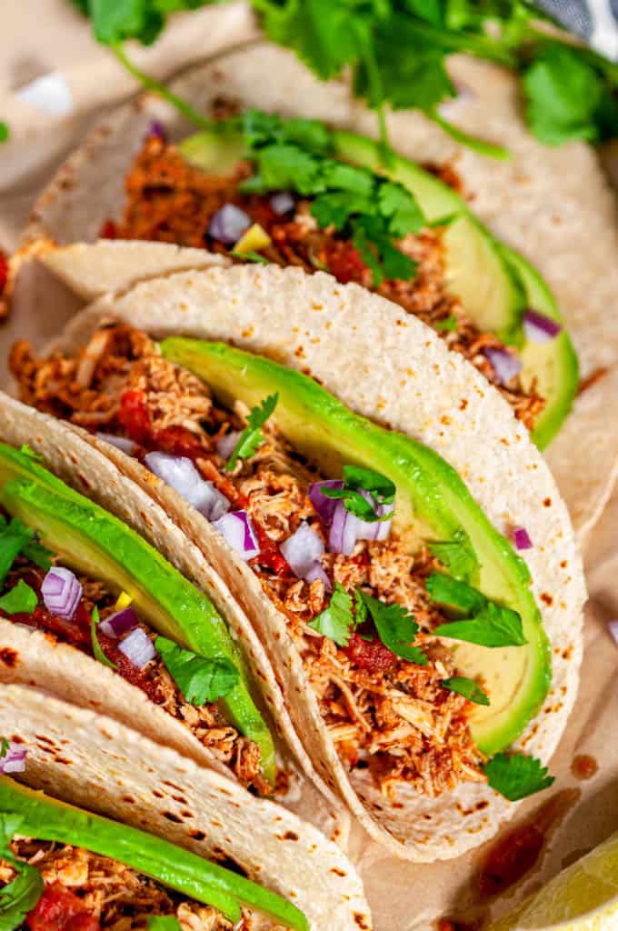 Instant Pot Chicken Tinga tacos with avocado, limes, red onion and cilantro on brown parchment close up