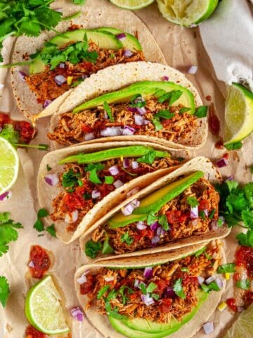 Instant Pot Chicken Tinga tacos with avocado, limes, red onion and cilantro on brown parchment over head