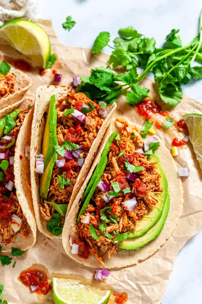 Instant Pot Chicken Tinga tacos with avocado, limes, red onion and cilantro on brown parchment
